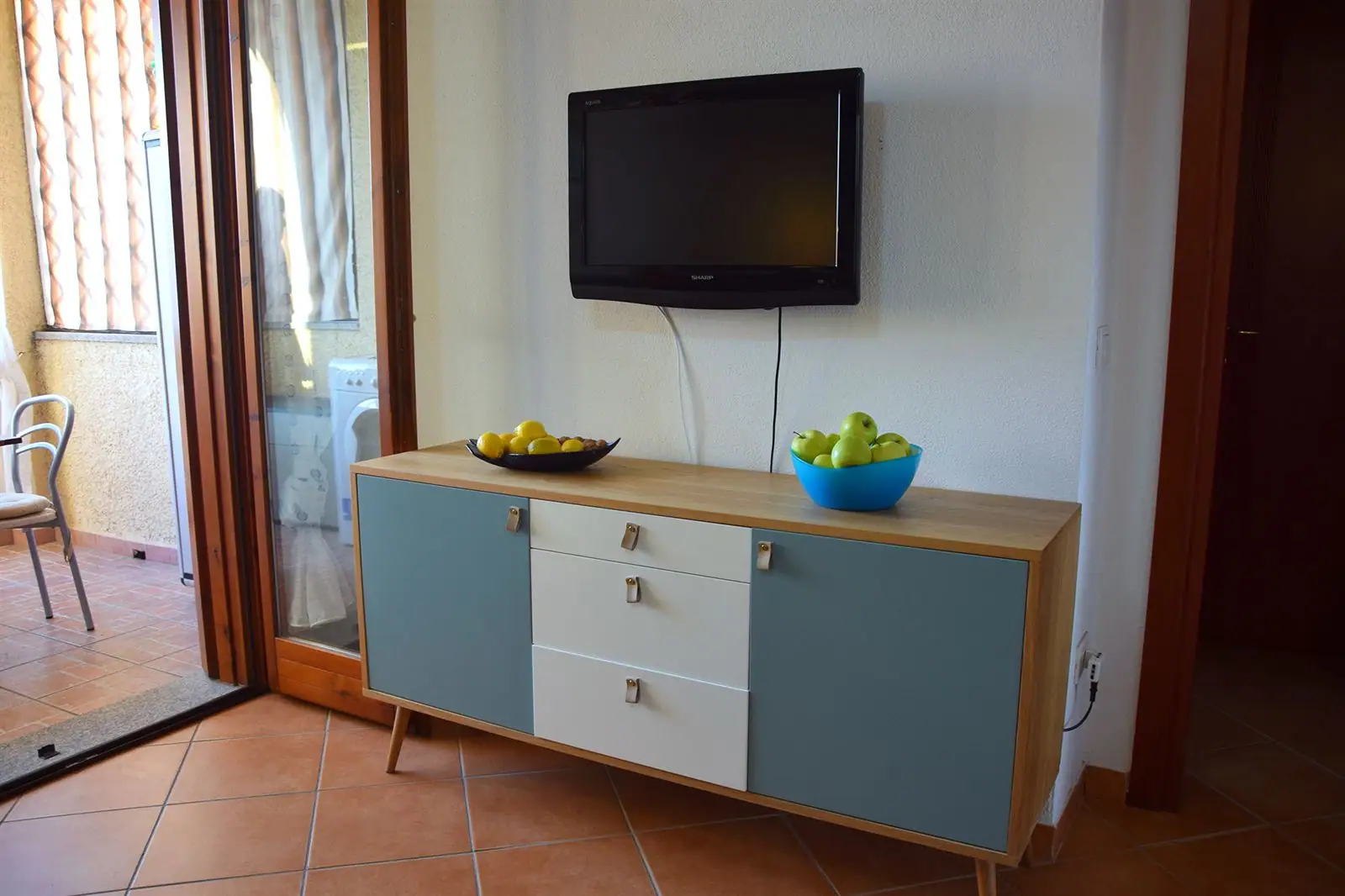 Wohnzimmer mit Fernseher und Zugang zum Balkon